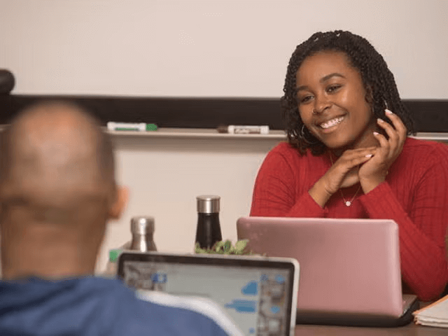 A student smiling with another student in front of her laptop